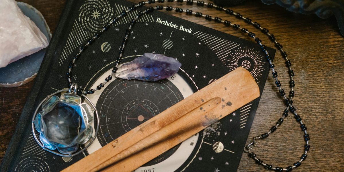 Astrology-themed flat lay featuring a birthdate book, crystals, and necklace on a wooden surface.
